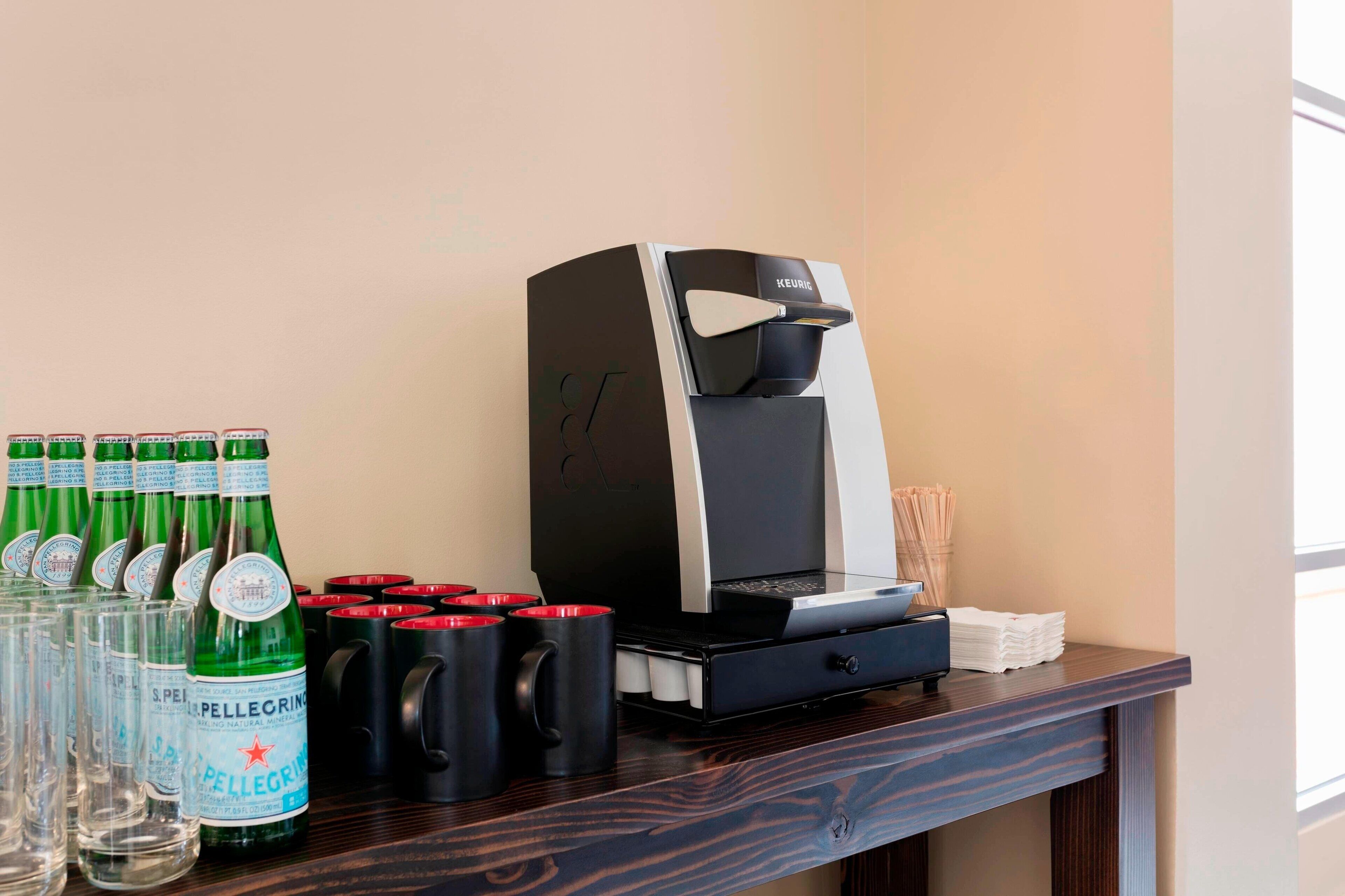 A coffee machine and bottles of Pellegrino water on a wooden counter.