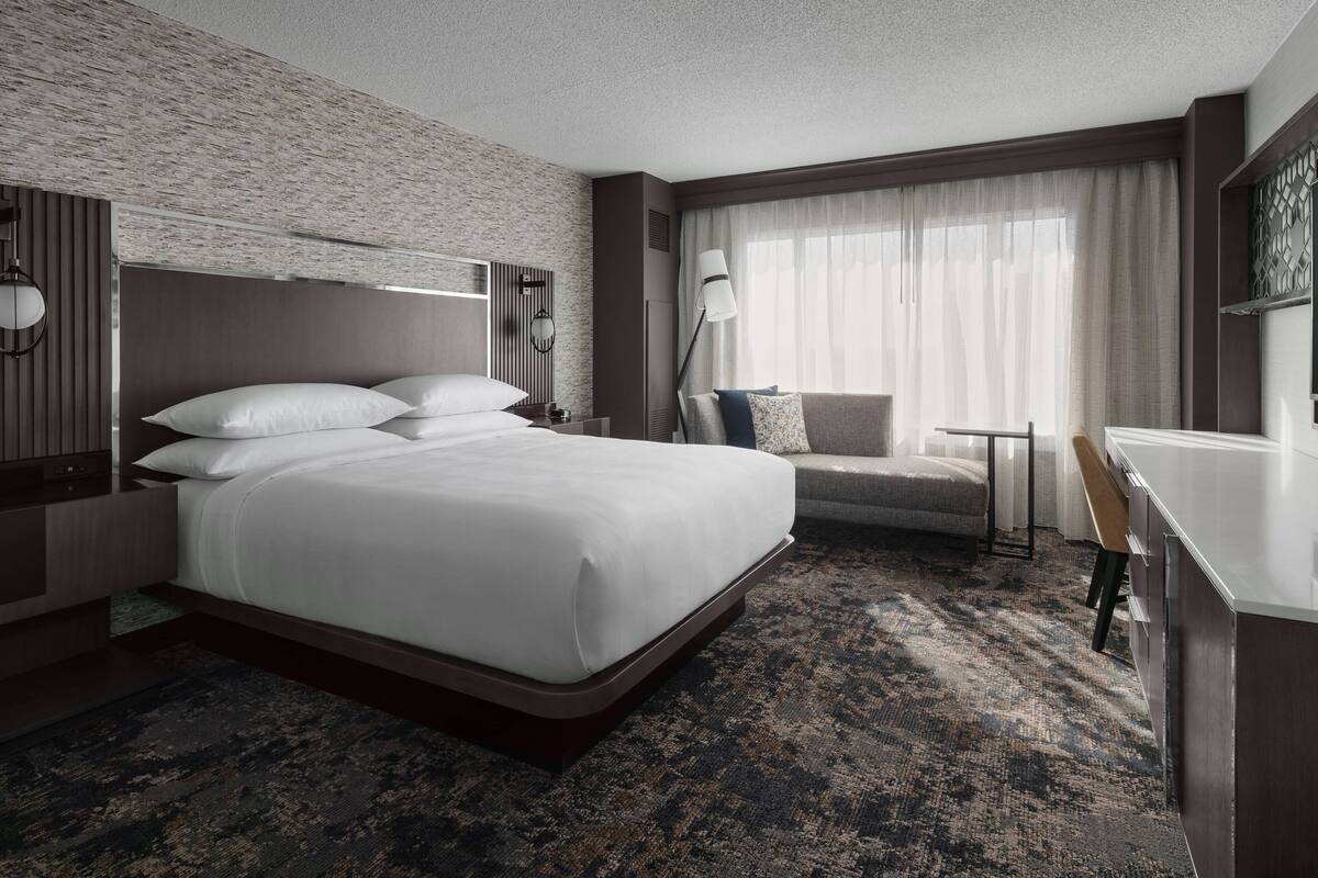 Una habitación de hotel moderna con una cama grande, un sofá, un escritorio y una ventana con cortinas.