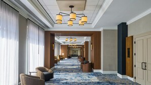A hotel lobby with a blue patterned carpet, modern lighting fixtures, and seating areas.