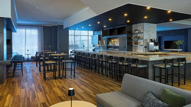A modern kitchen with a bar area, wooden flooring, and a grey sofa.