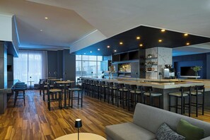 A modern kitchen with a bar area, wooden flooring, and a grey sofa.