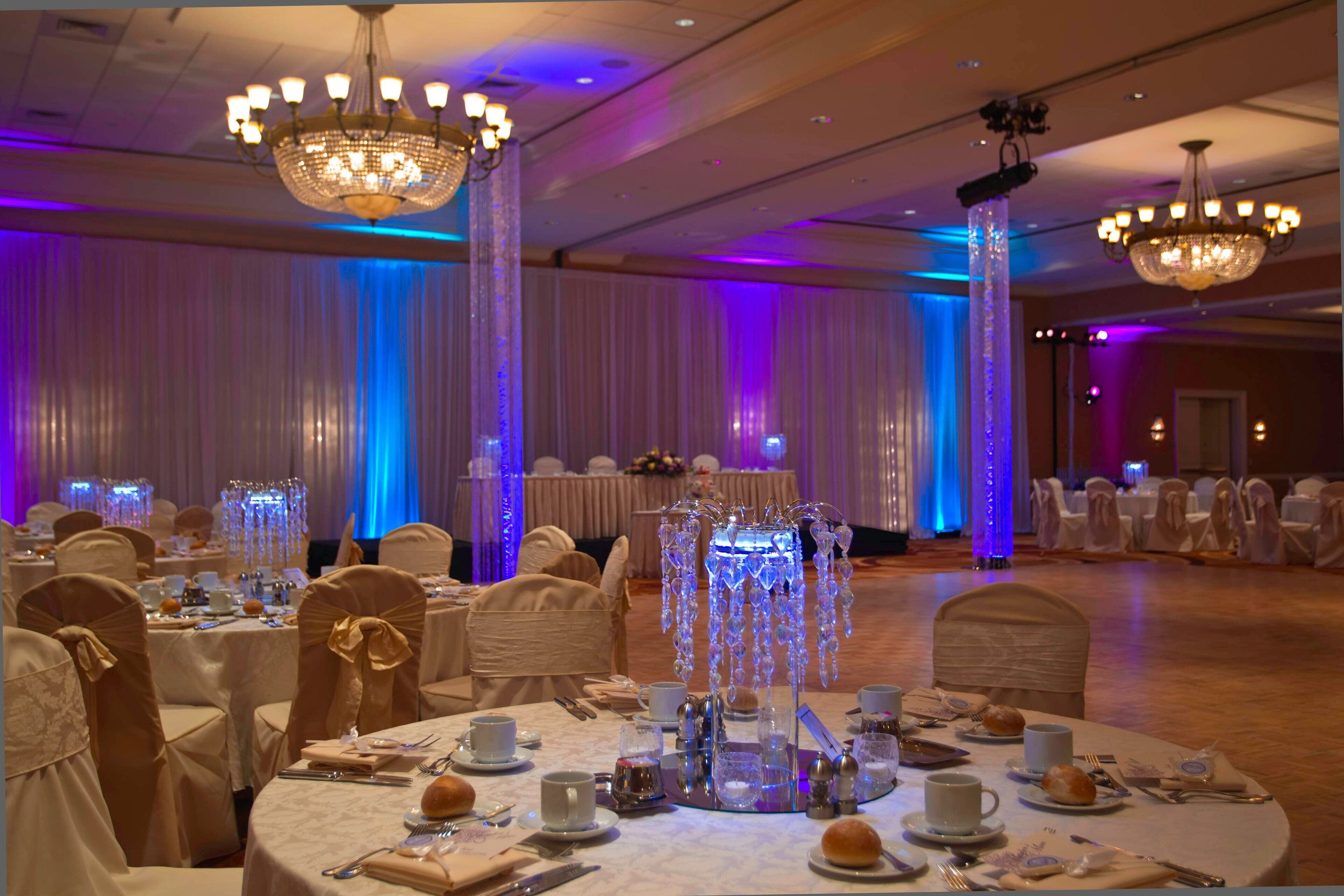 A banquet hall with round tables set for a formal event, adorned with crystal centerpieces and white tablecloths.