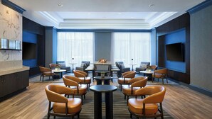 A spacious lounge area with multiple seating arrangements, a central table, and a television screen on the wall.