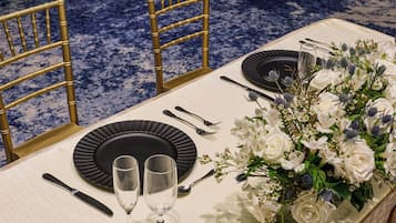 A table set with black plates, silverware, and two wine glasses, accompanied by a floral centerpiece.