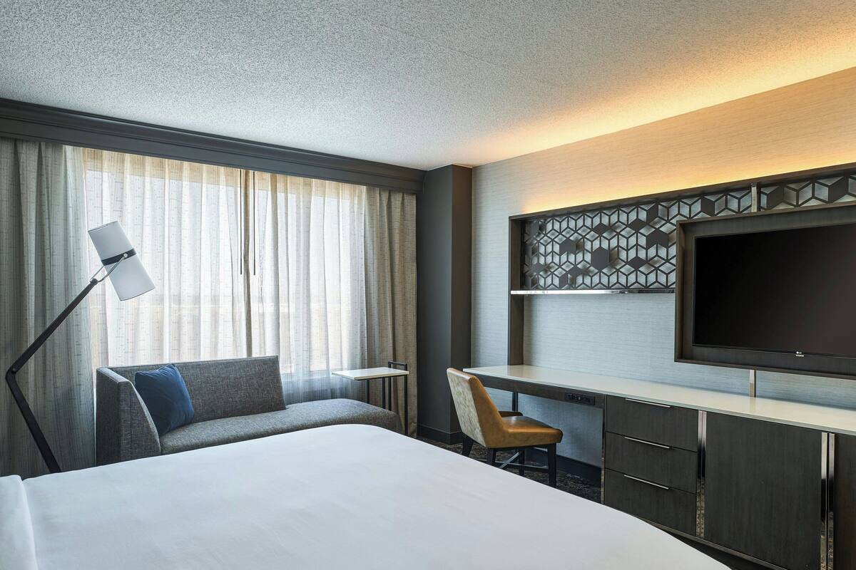 Una habitación de hotel con una cama grande, un escritorio, una silla, un televisor y una ventana con cortinas.