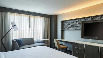 A hotel room with a large bed, a desk, a chair, a TV, and a window with curtains.
