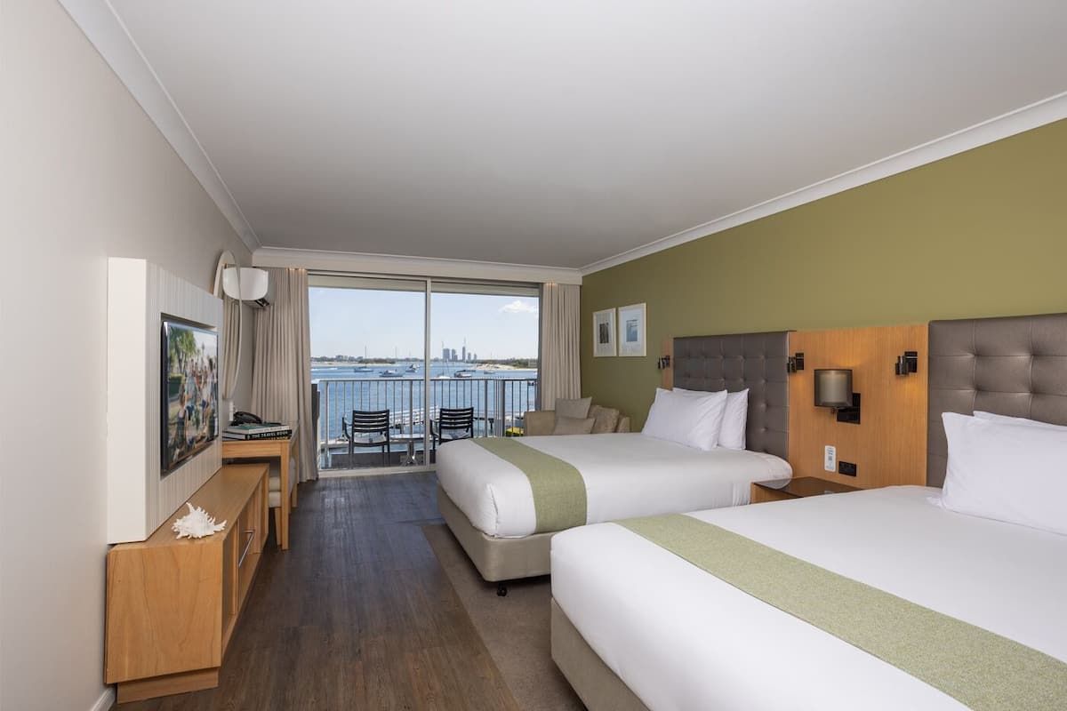 A hotel room with two beds, a desk, a chair, and a balcony with a view of the water.