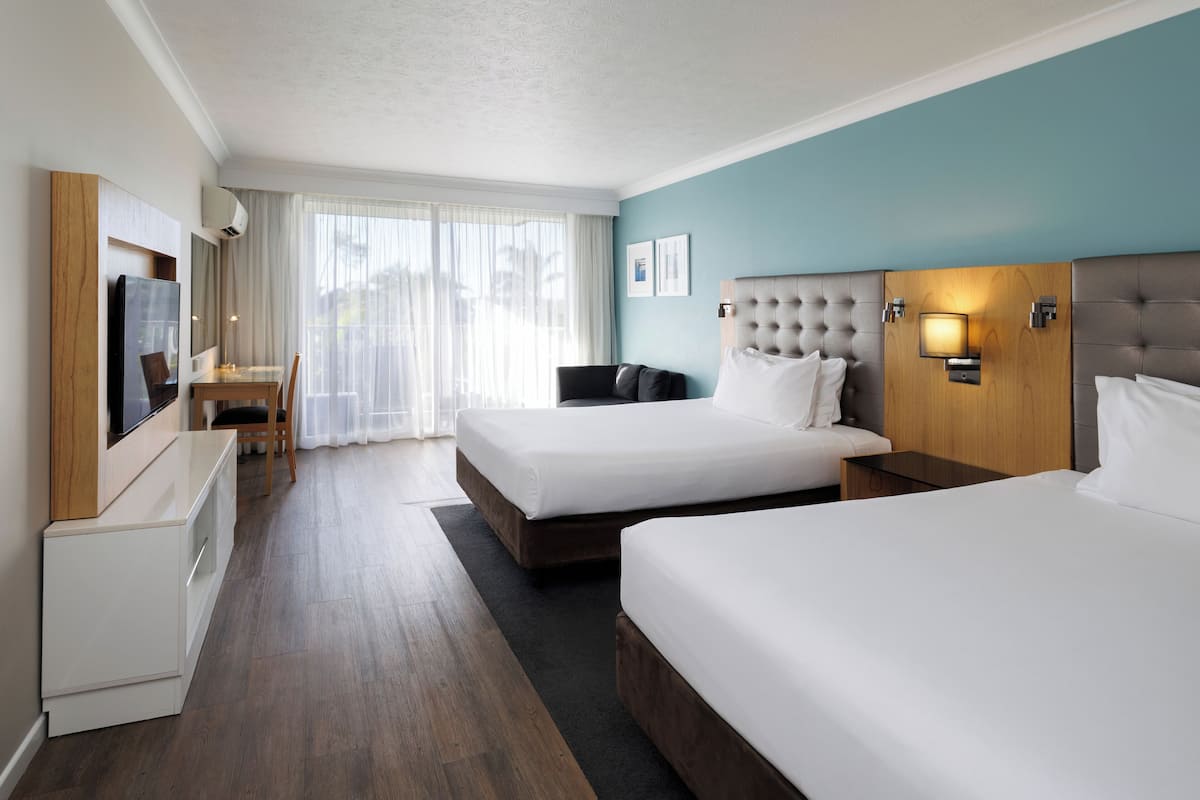A hotel room with two beds, a desk, a chair, a TV, and a window with curtains.