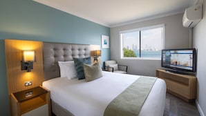 Habitación de hotel con una cama grande, televisor, ventana con vista a la ciudad y mesita de noche con lámpara.