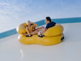 Two people sitting on a large yellow inflatable tube on a white surface with a blue sky in the background.