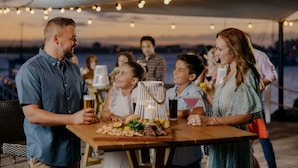 Un grupo de personas cenando en una mesa al aire libre, con luces colgantes.