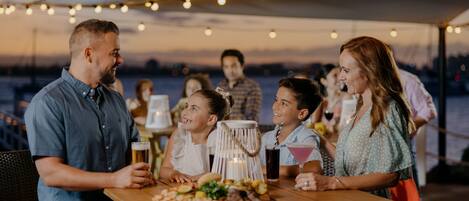 A group of people dining at an outdoor table with string lights overhead.