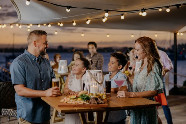 Un grupo de personas cenando en una mesa al aire libre, con luces colgantes.