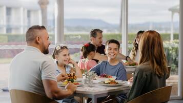 Un grupo de personas cenando en una mesa con vistas a montañas y vegetación.