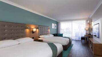 Habitación de hotel con dos camas, un escritorio y vistas de la ciudad a través de amplios ventanales.