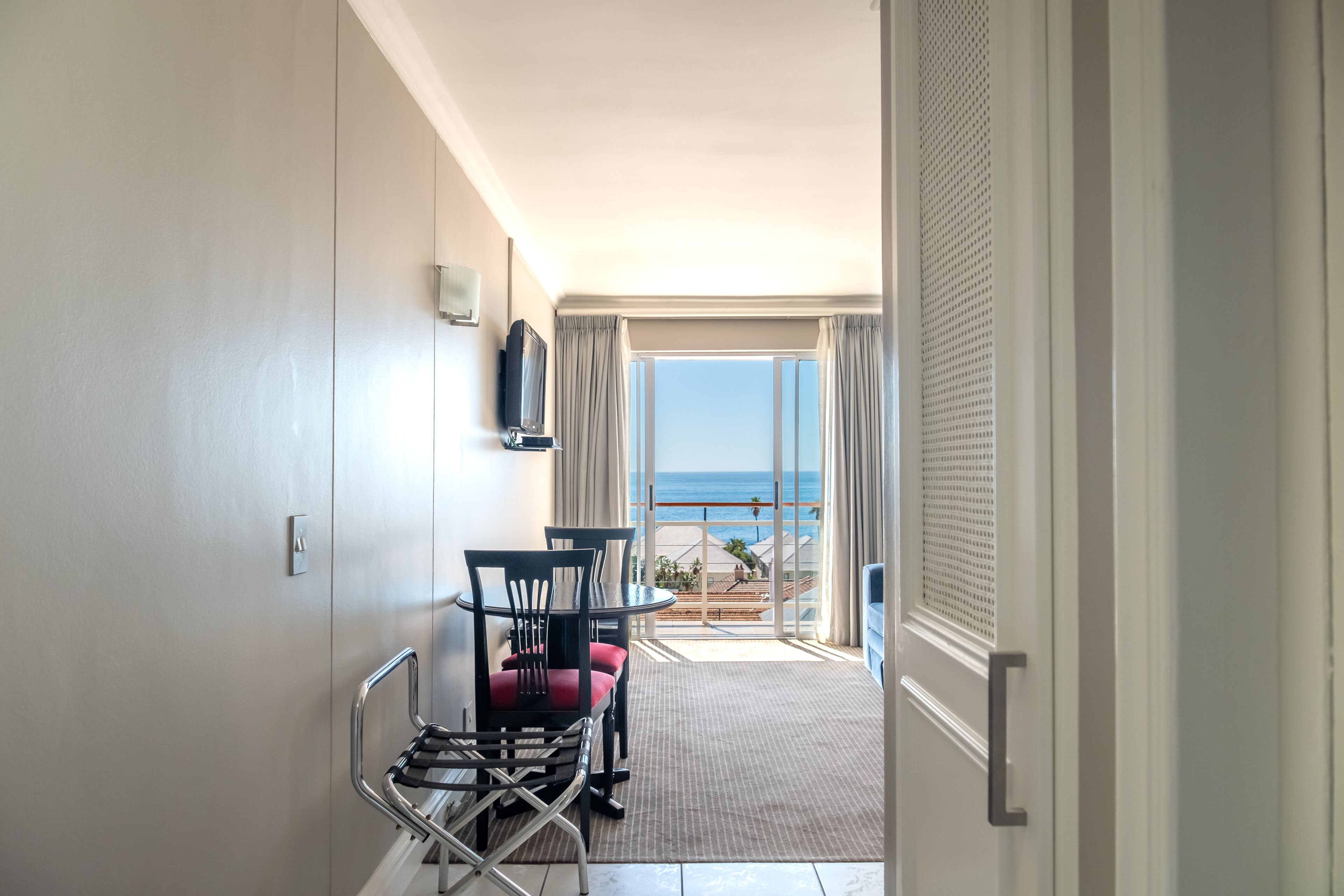 Habitación de hotel con balcón, zona de comedor con sillas y mesa, y televisor montado en la pared.