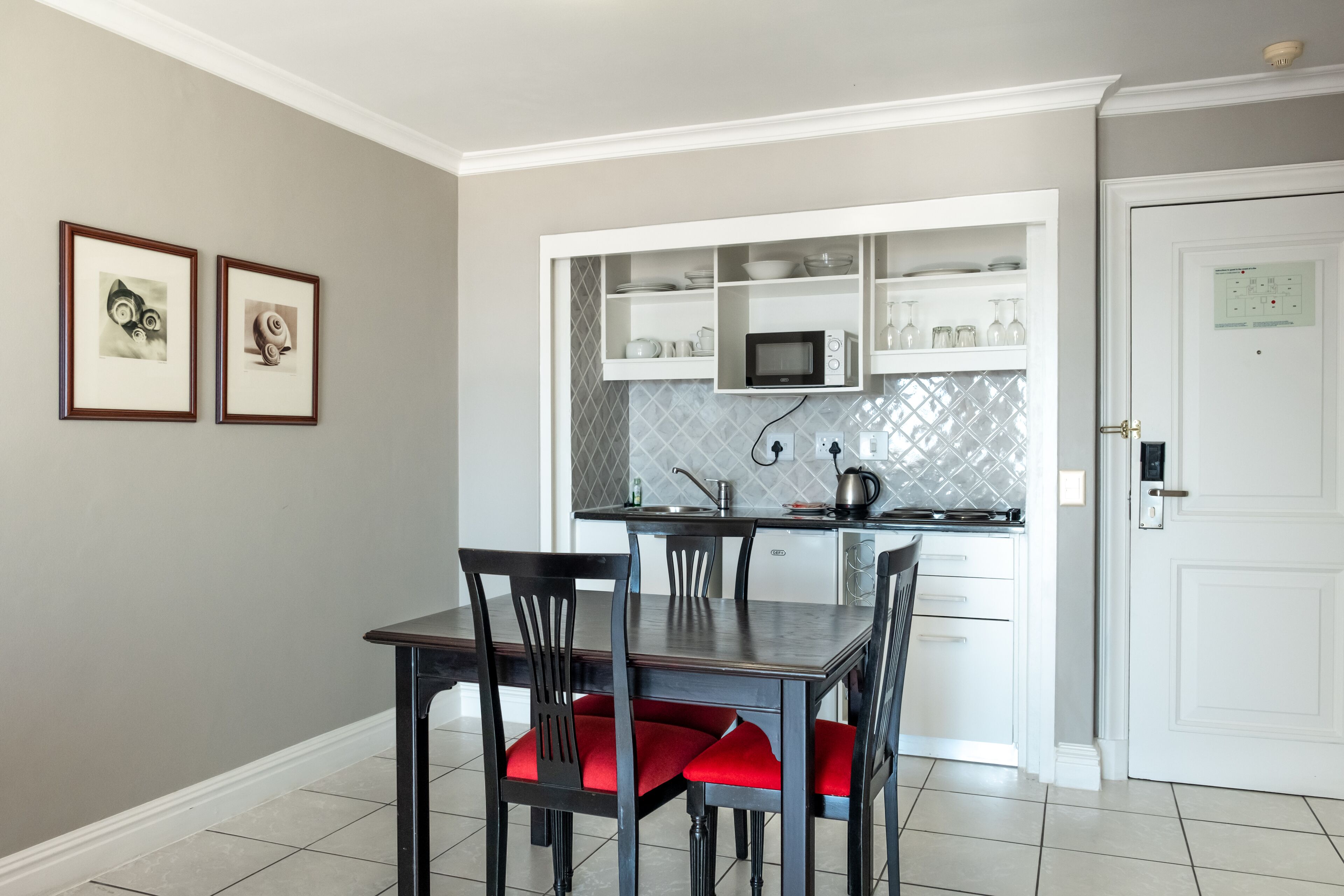 A dining area with a table and chairs, a kitchen with white cabinets and a microwave, and a door with a lock.
