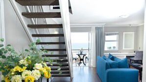 A modern living room with a blue sofa, a staircase, and a view of the sea. - The Bantry Bay Aparthotel by Totalstay (Cape Town)