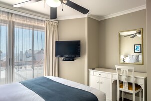 A hotel room with a bed, a desk, a chair, a television, and a balcony with curtains.
