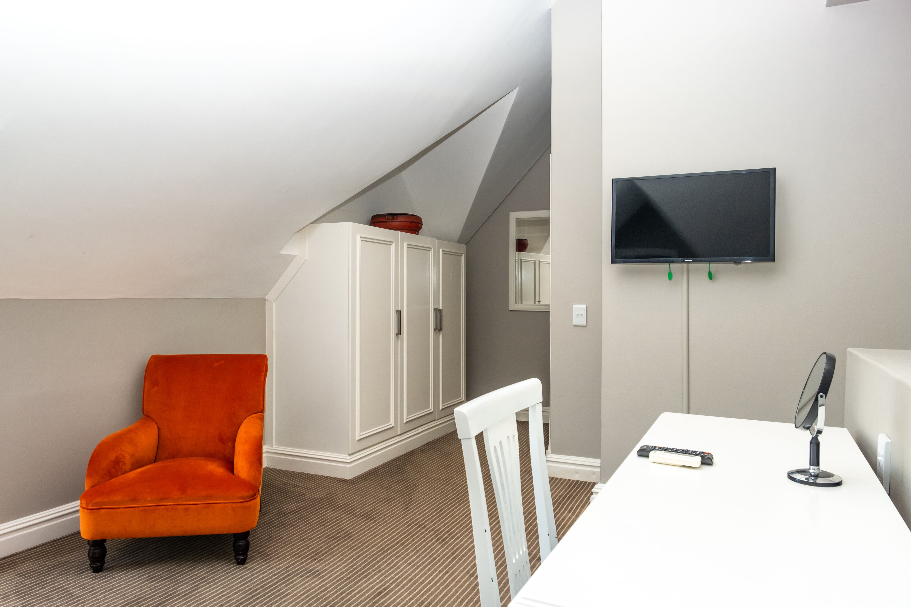 Une pièce comprenant une table blanche, une chaise blanche, une chaise rouge, un téléviseur et un meuble.