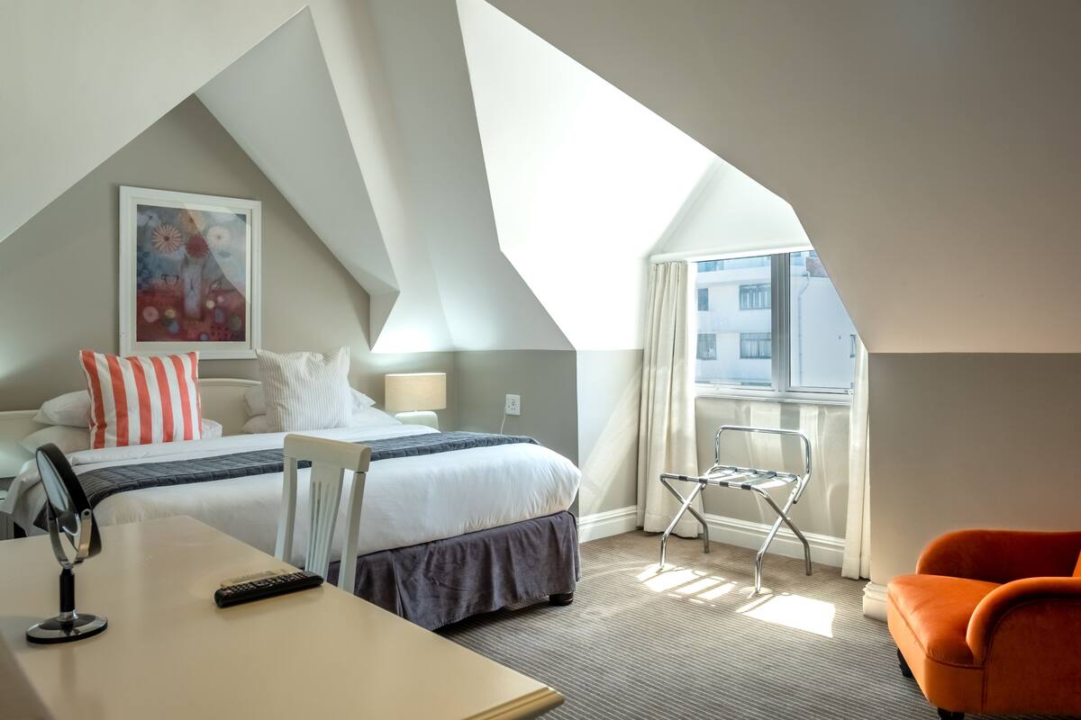 Ett modernt hotellrum med två sängar, ett skrivbord, en stol och ett fönster med gardiner.