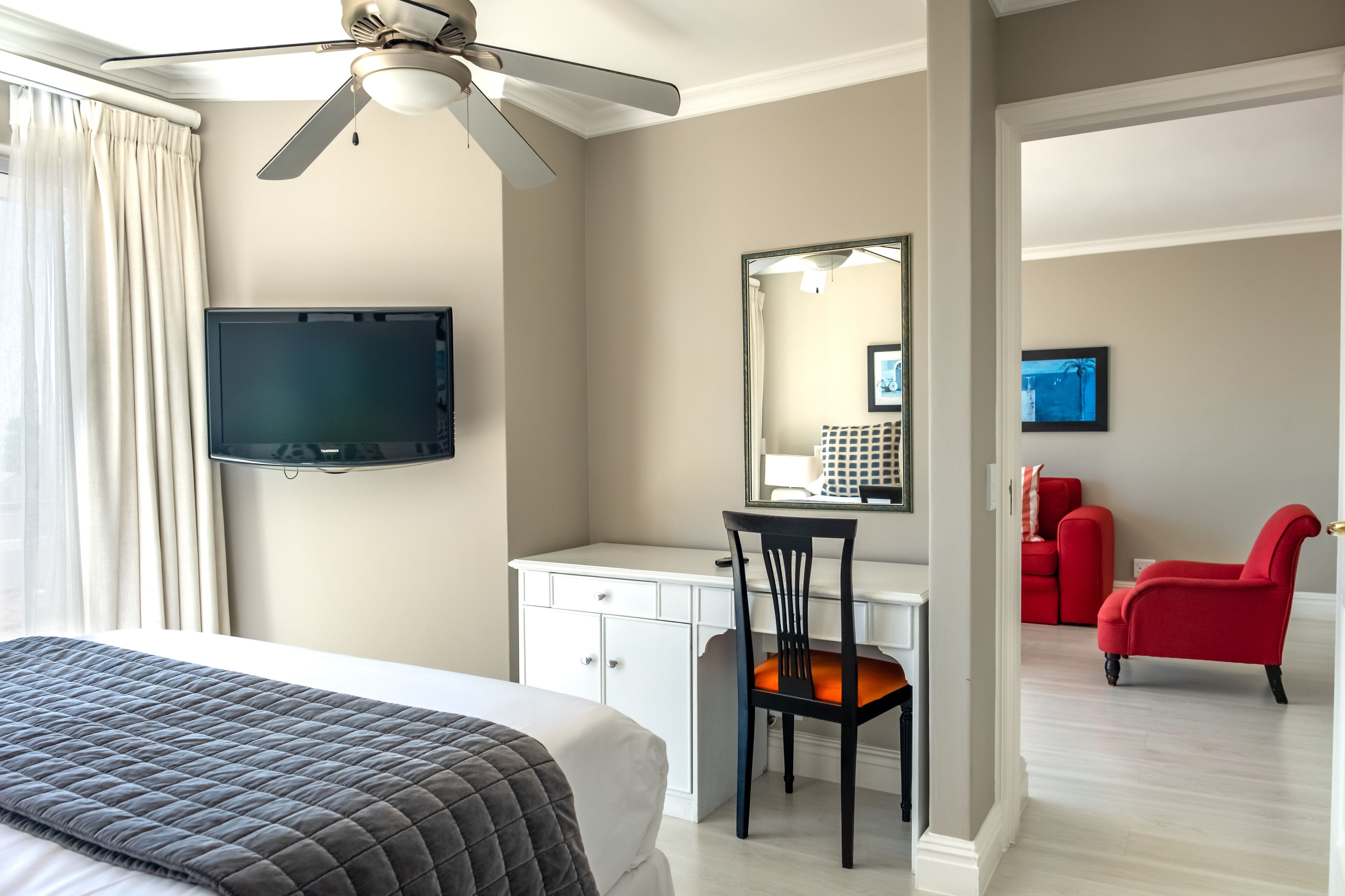 Habitación de hotel con cama, escritorio, silla, televisor y sillón rojo.