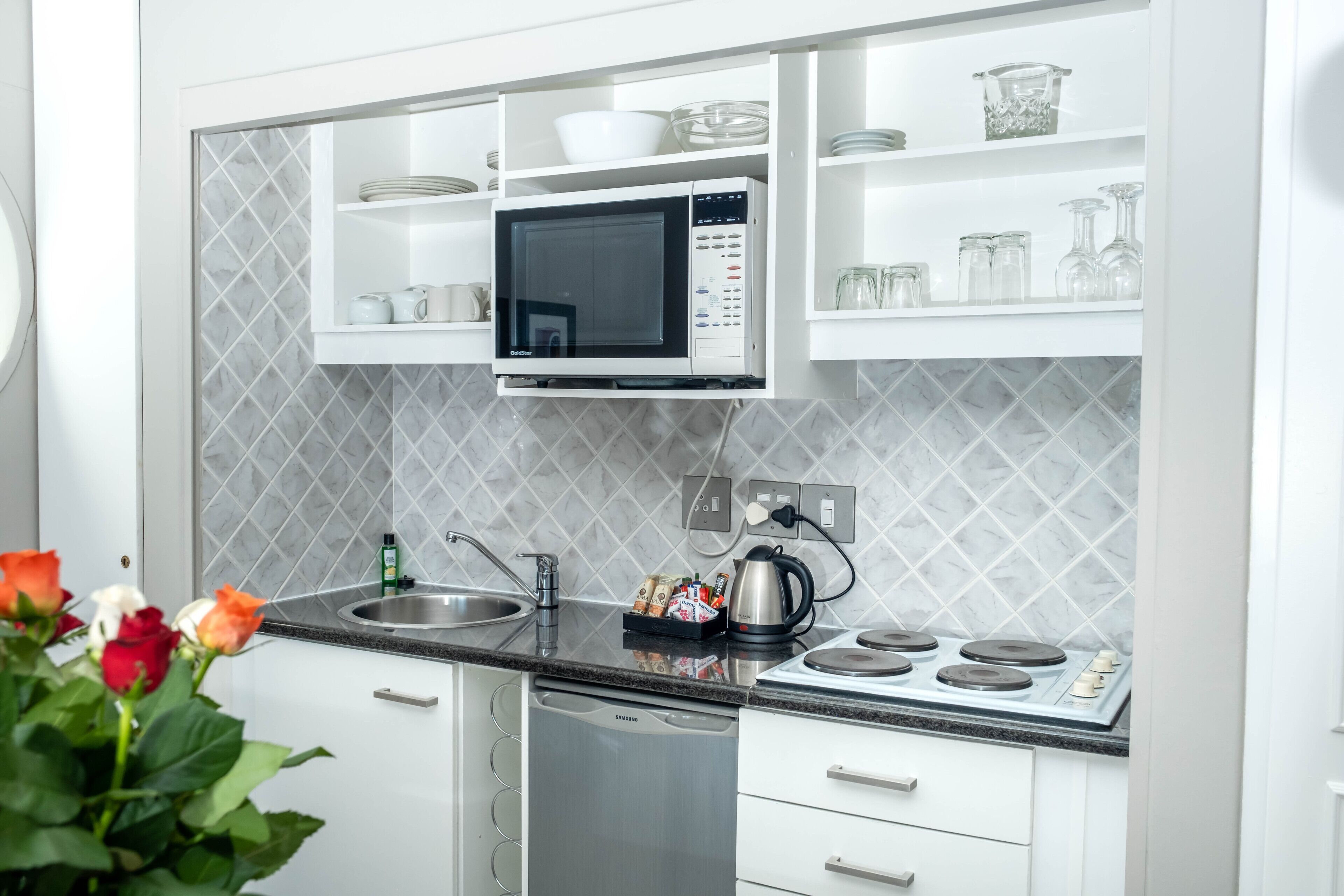 Una cucina moderna con mobili bianchi, un forno a microonde integrato, un piano cottura ed una lavastoviglie.