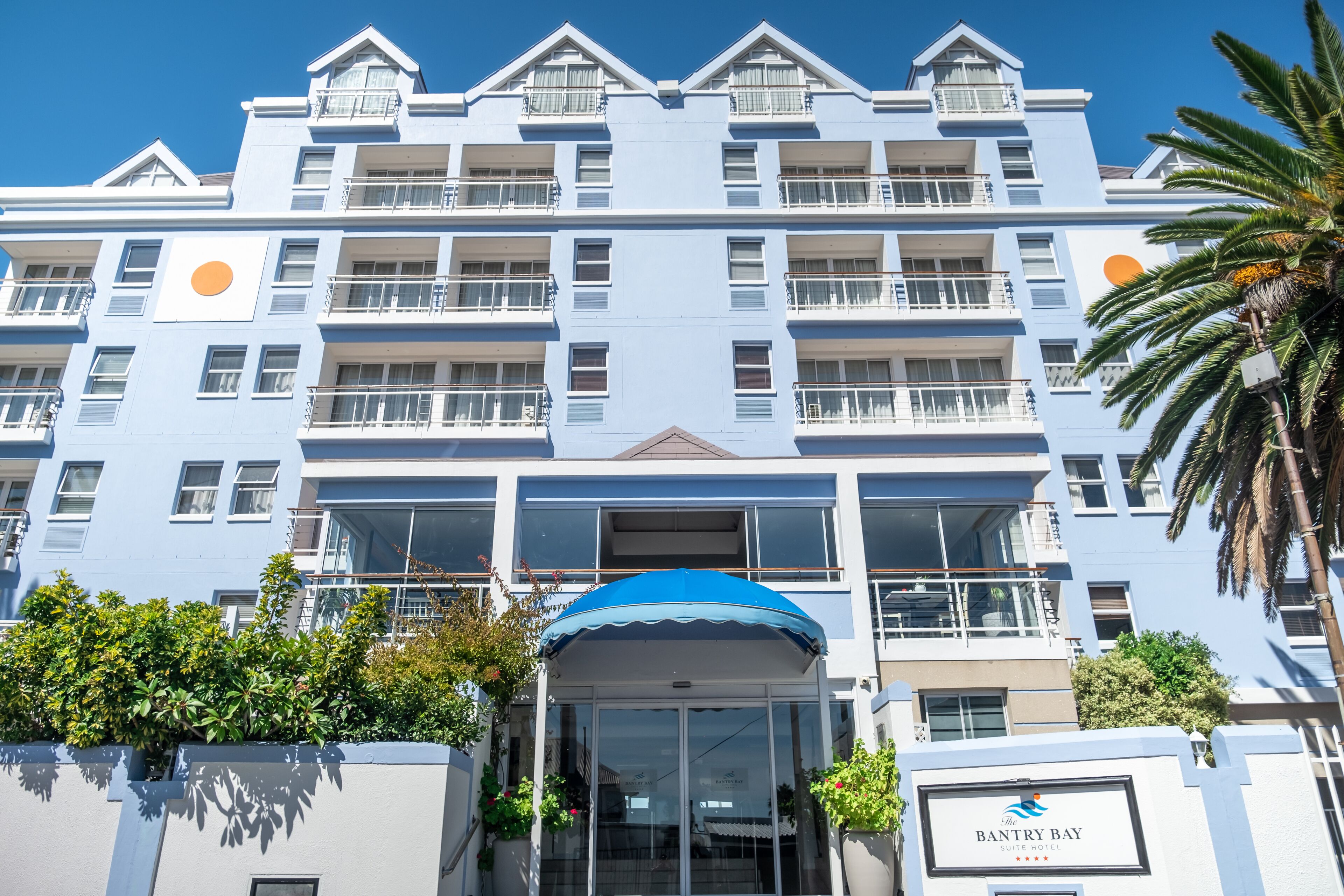A multi-story hotel with balconies, a blue awning, and a palm tree in the foreground.