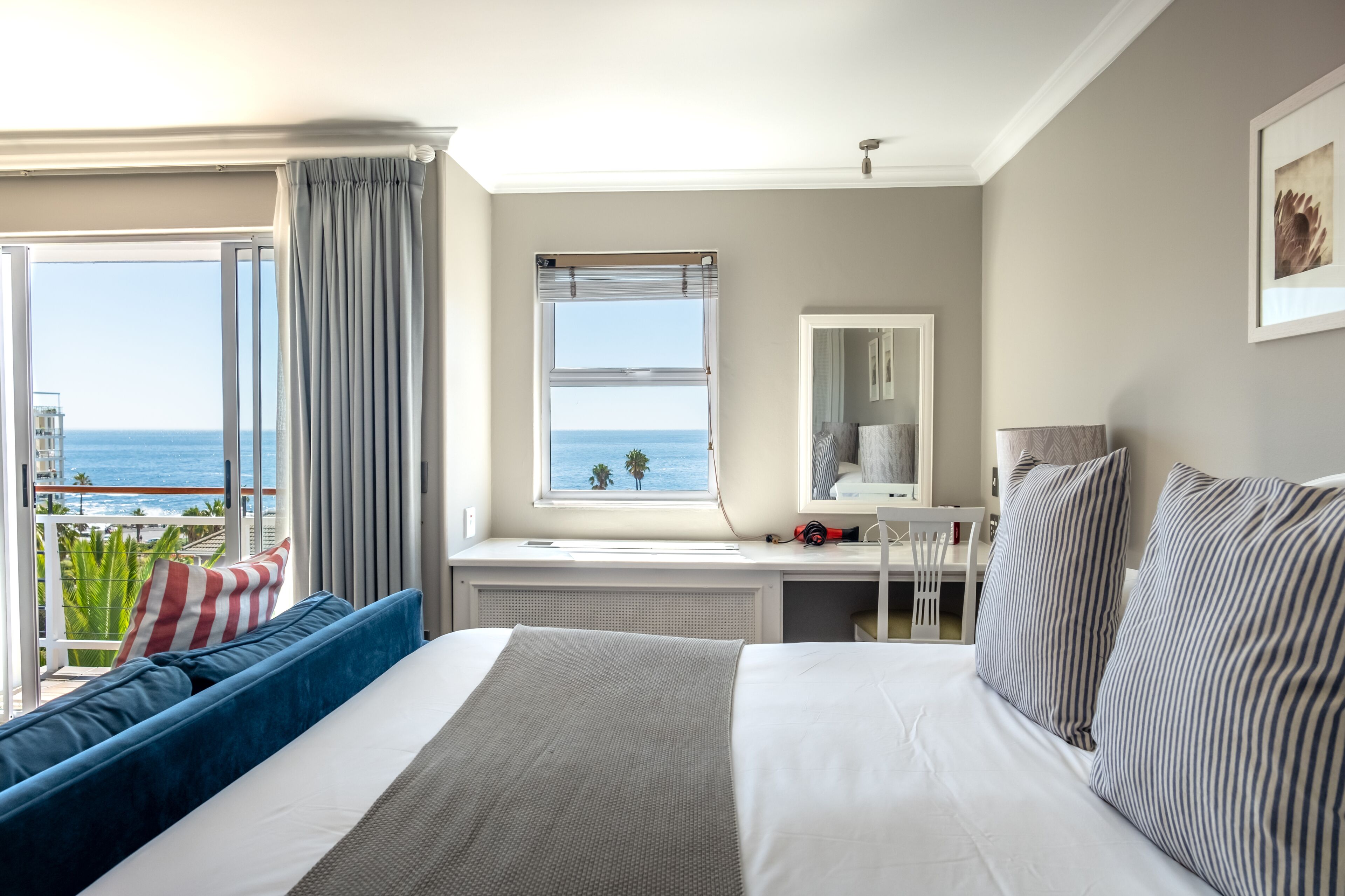 A hotel room with a large bed, a desk, a chair, a window with a view of the ocean, and a balcony with a view of the ocean.