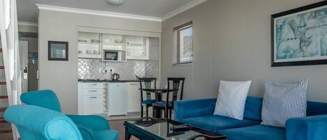A living room with a blue sofa, matching armchairs, a coffee table, and a kitchen in the background.
