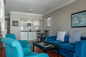 A living room with a blue sofa, matching armchairs, a coffee table, and a kitchen in the background.