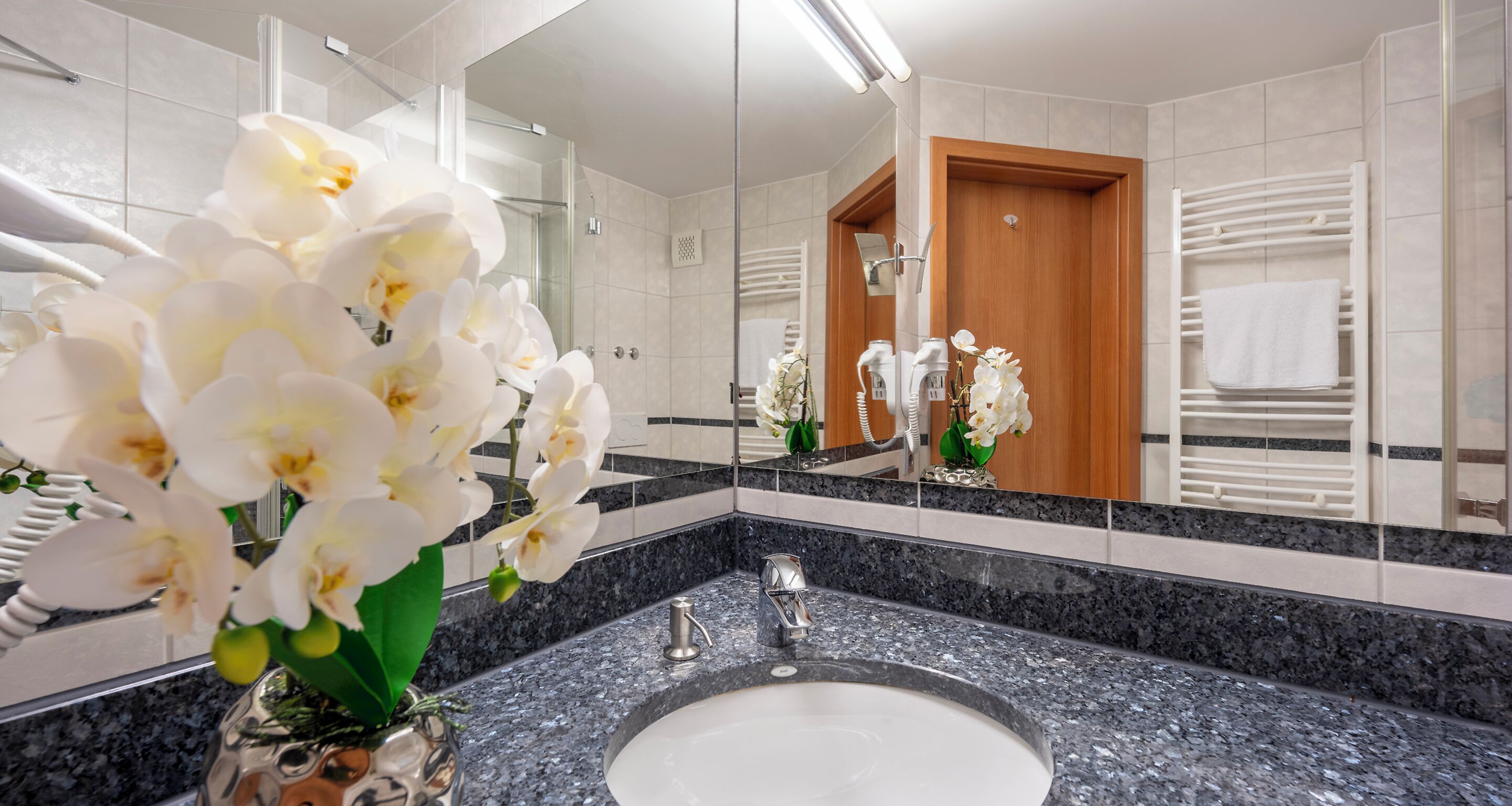 A modern bathroom with a granite countertop, a sink, a mirror, and white orchids.