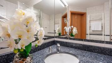 A modern bathroom with a granite countertop, a sink, a mirror, and white orchids.