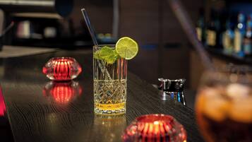 Un bar avec un verre contenant une boisson décorée d’une tranche de citron vert et de feuilles de menthe, un objet décoratif rouge et un récipient en métal posé sur le comptoir.