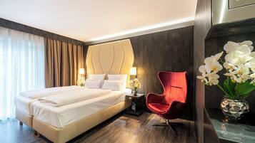 A hotel room with a large bed, a red chair, a vase with white flowers, and a modern wall design.