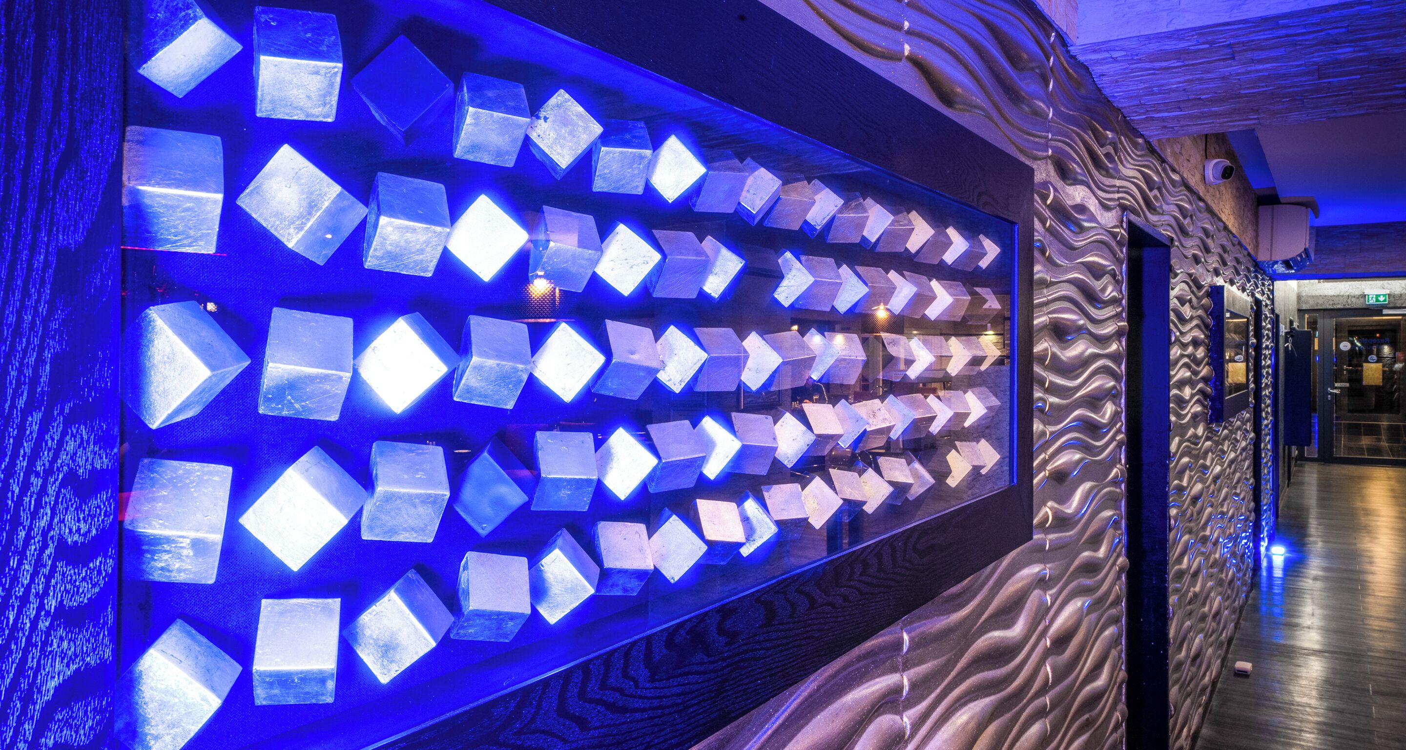 A hallway with a wall of illuminated geometric shapes and a textured wall design.
