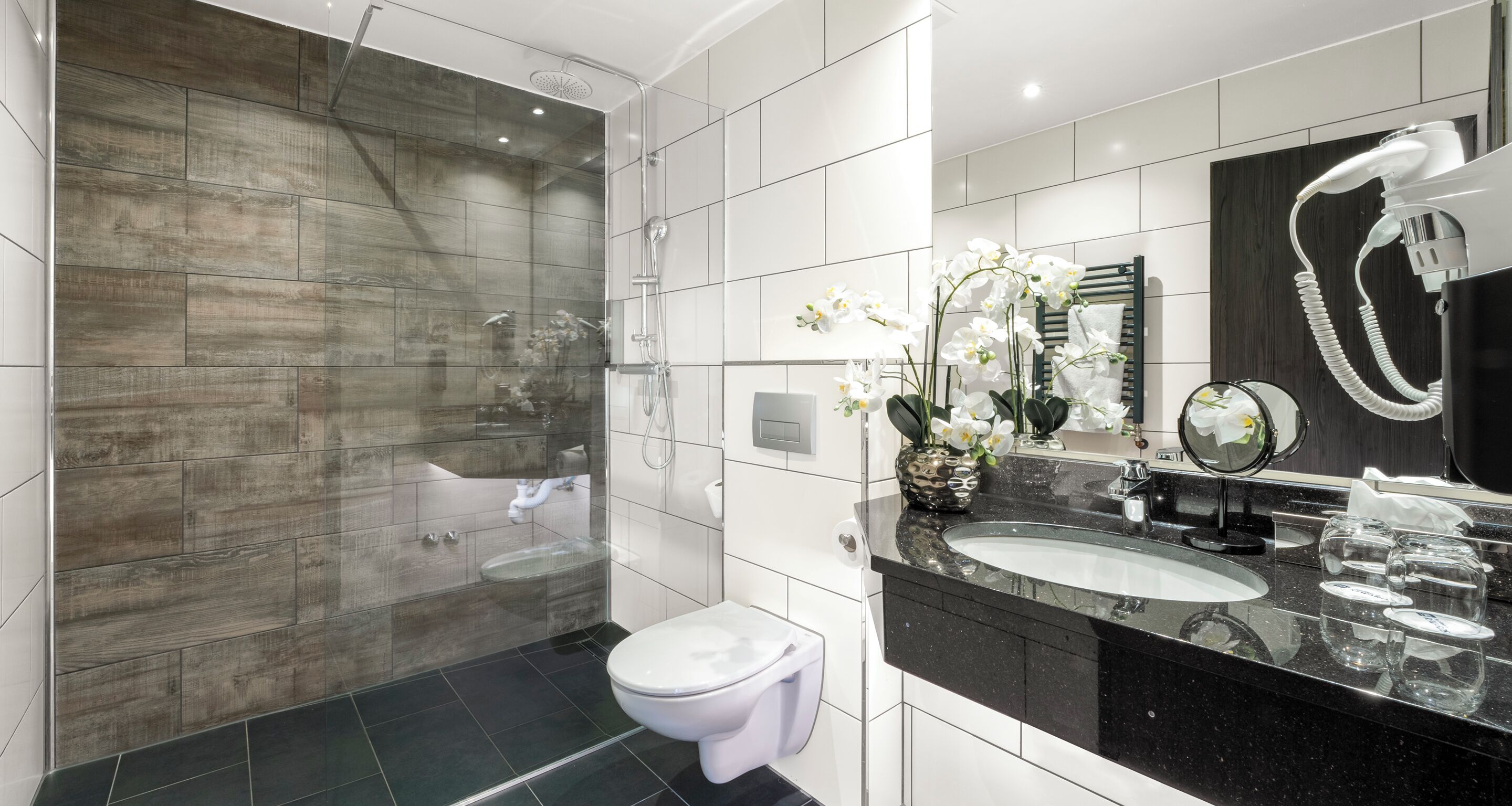 A modern bathroom with a glass-enclosed shower, a white toilet, a black countertop with a sink, and a mirror.
