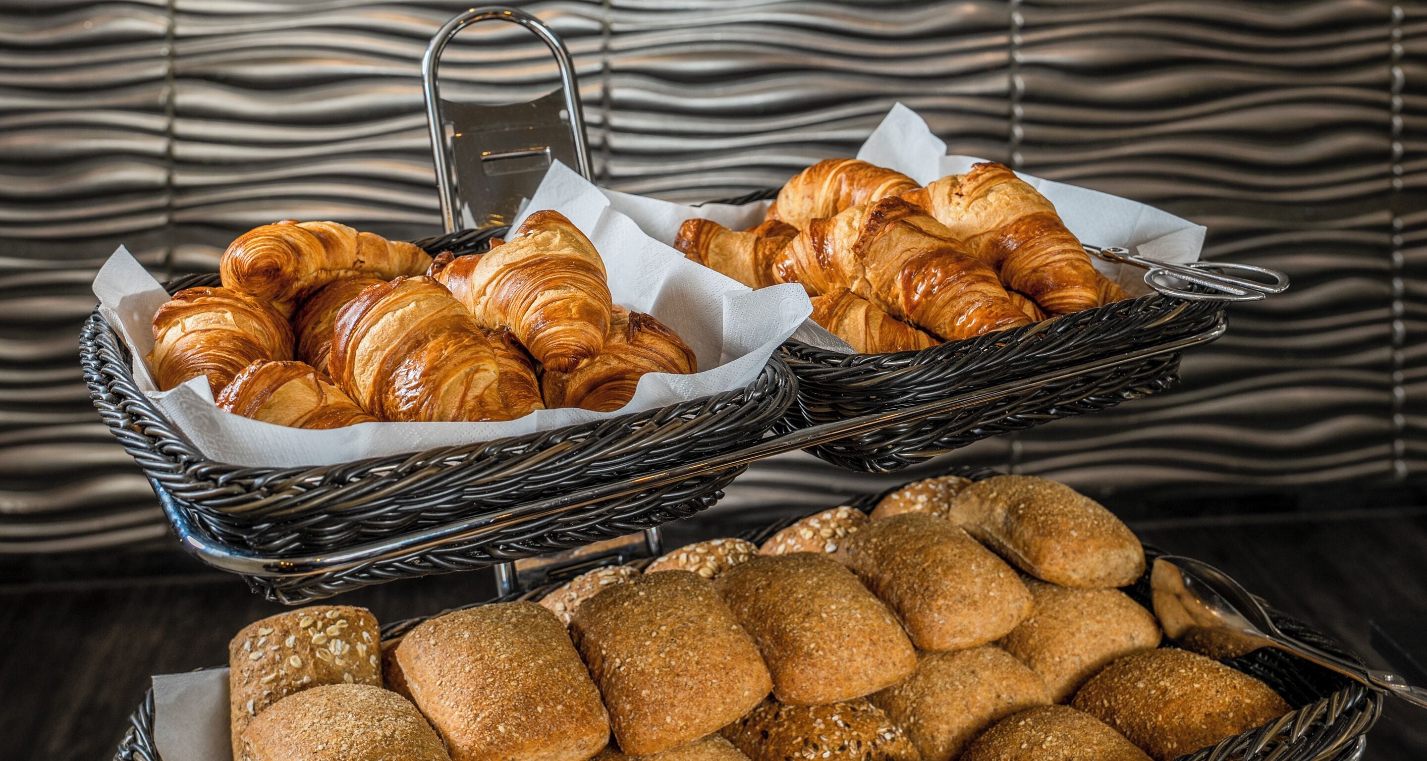 Two baskets of croissants and bread on a table.