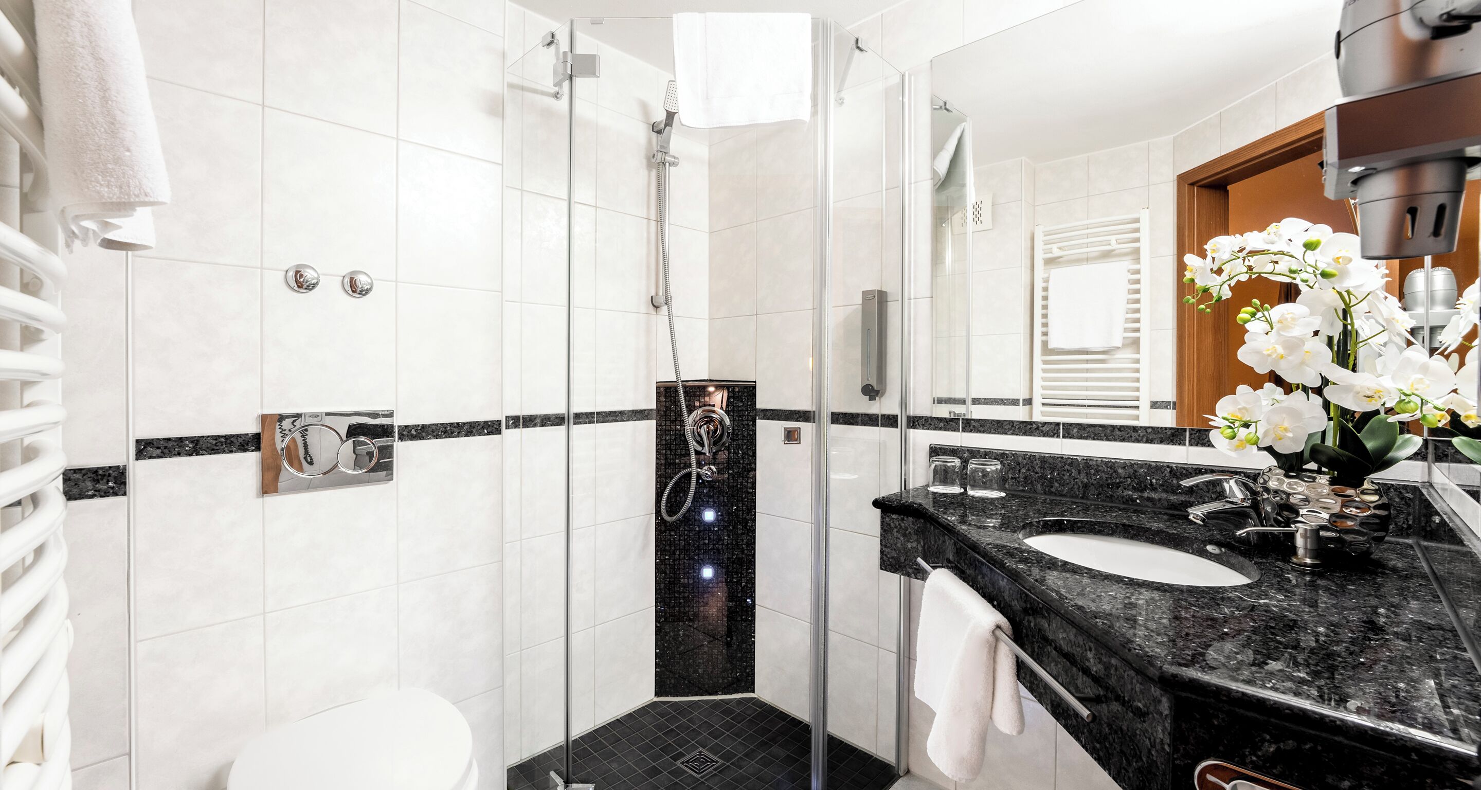 Un baño moderno con ducha envuelta en vidrio, lavamanos de mármol negro y azulejos blancos.