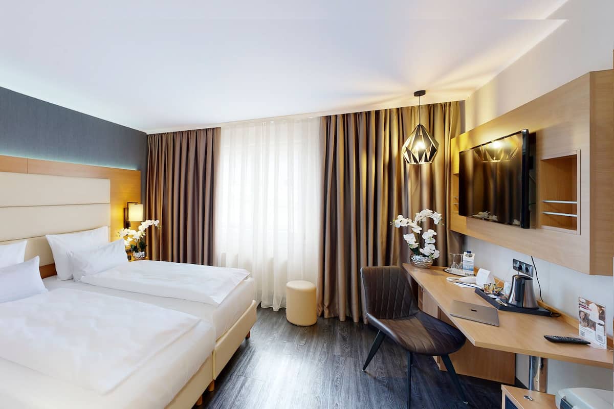 A hotel room with two beds, a desk, a chair, a TV, and a lamp.