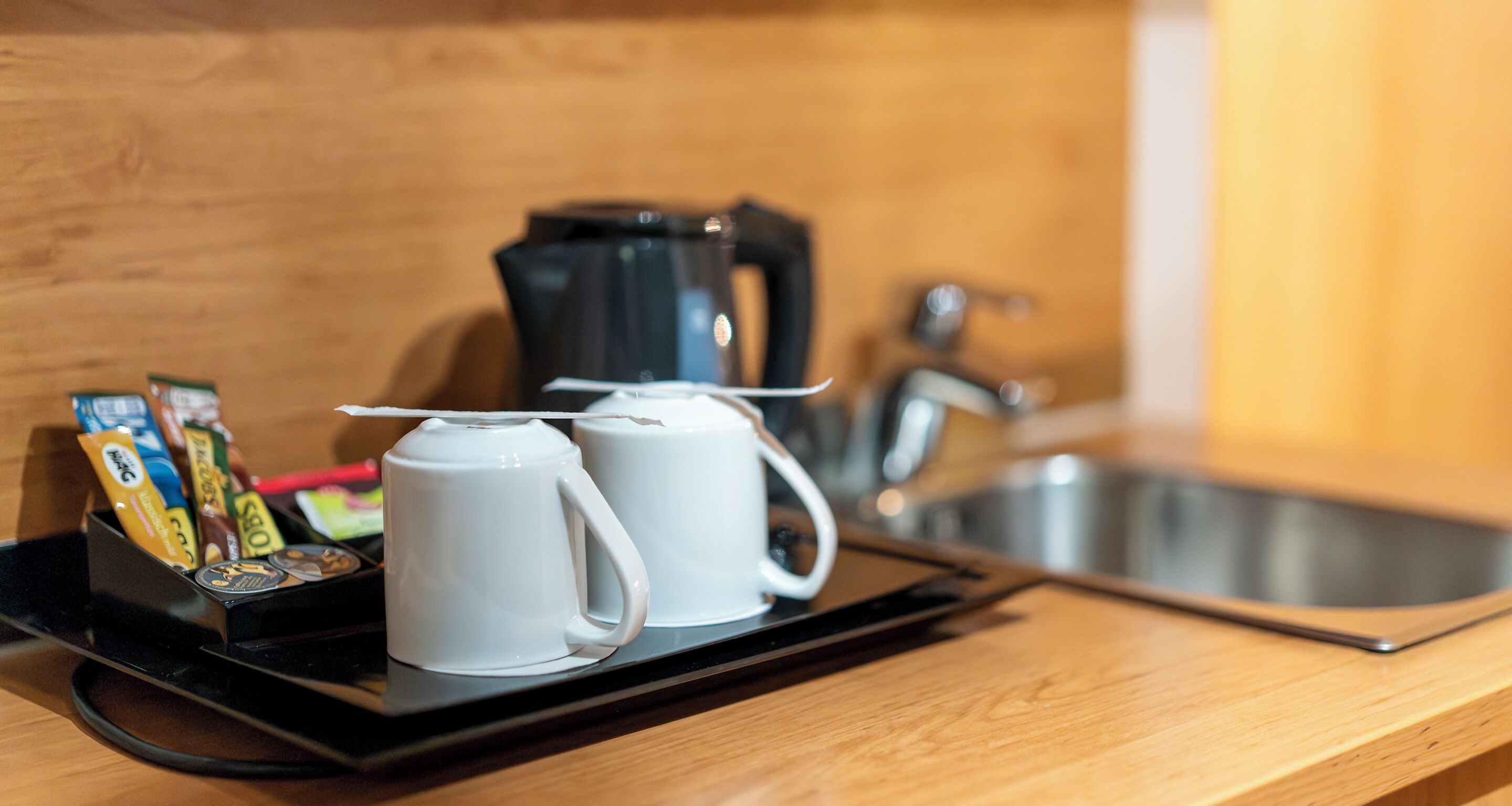 Uma bandeja com canecas de café e uma cafeteira em uma bancada de madeira.