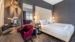 A hotel room with a bed, a desk with a laptop, a red chair, a mirror, and a vase with flowers. - PLAZA INN Heilbronn (Heilbronn)