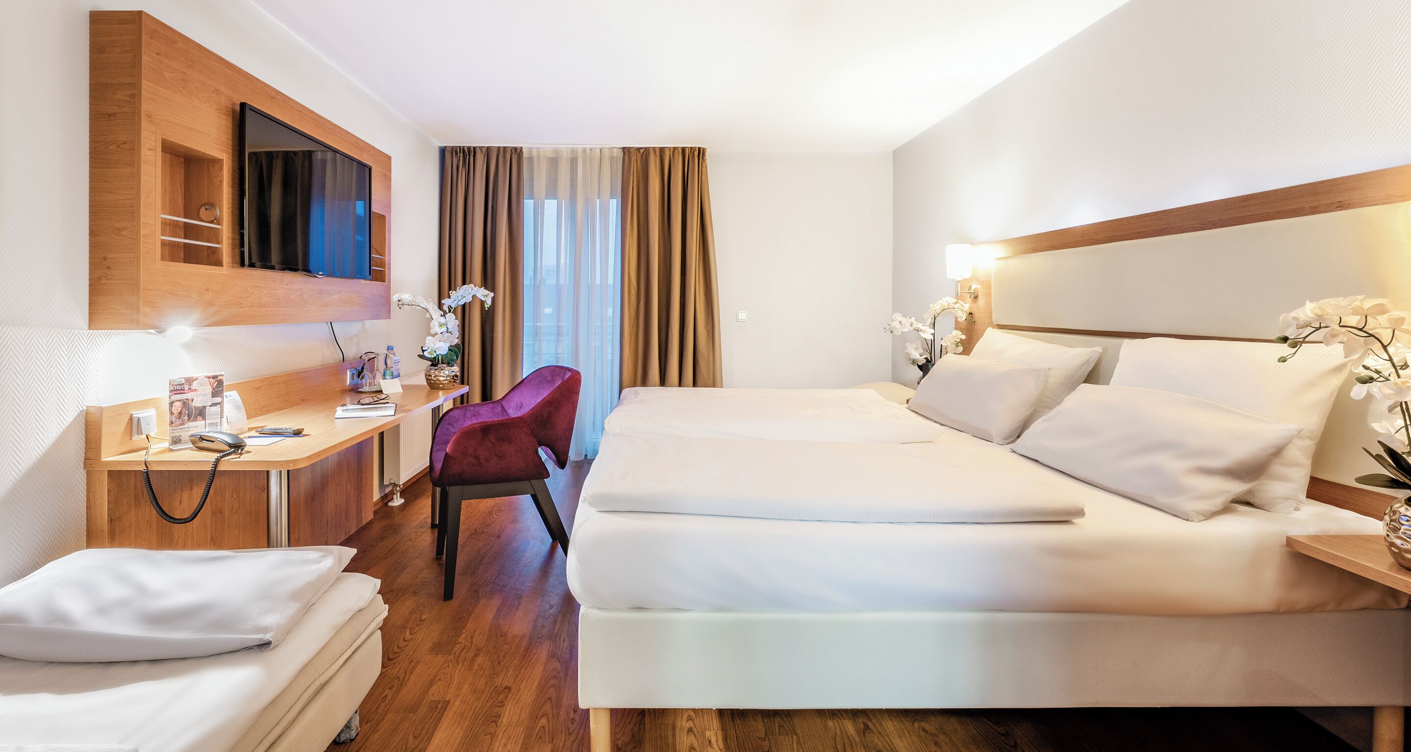 A hotel room with two beds, a desk with a telephone, a chair, and a TV mounted on the wall.