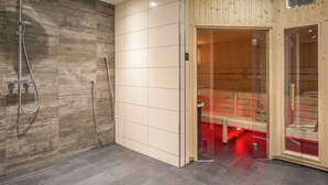 A modern sauna with a wooden interior, a glass door, and a shower area with a metal hose. - PLAZA INN Heilbronn (Heilbronn)