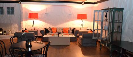 A cozy living room with a round coffee table, two sofas with orange cushions, and a dining area with a round table and chairs.