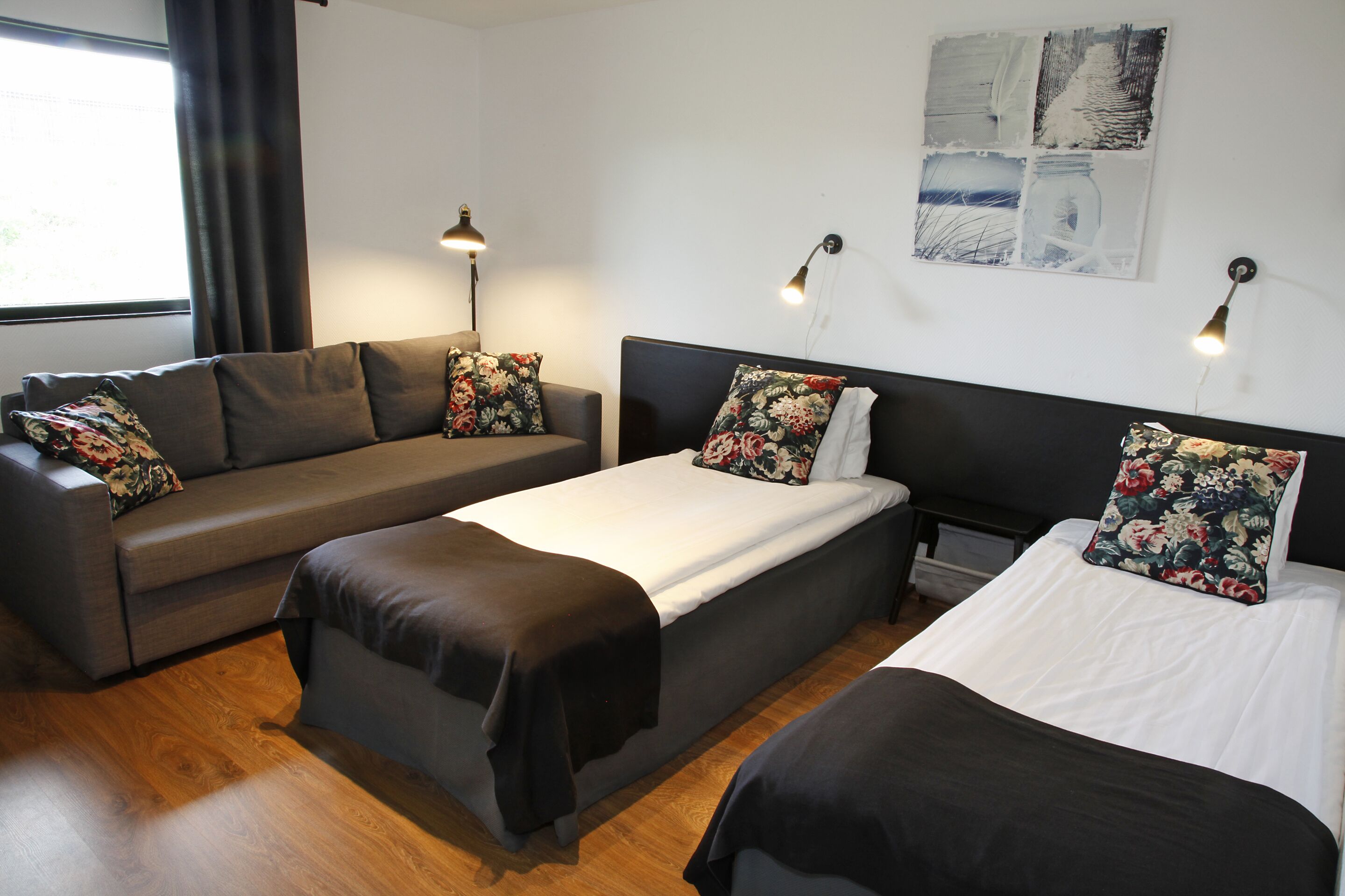 A room with a sofa, a bed, and a nightstand. There are two lamps on the wall.