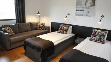 A room with a sofa, a bed, and a nightstand. There are two lamps on the wall.