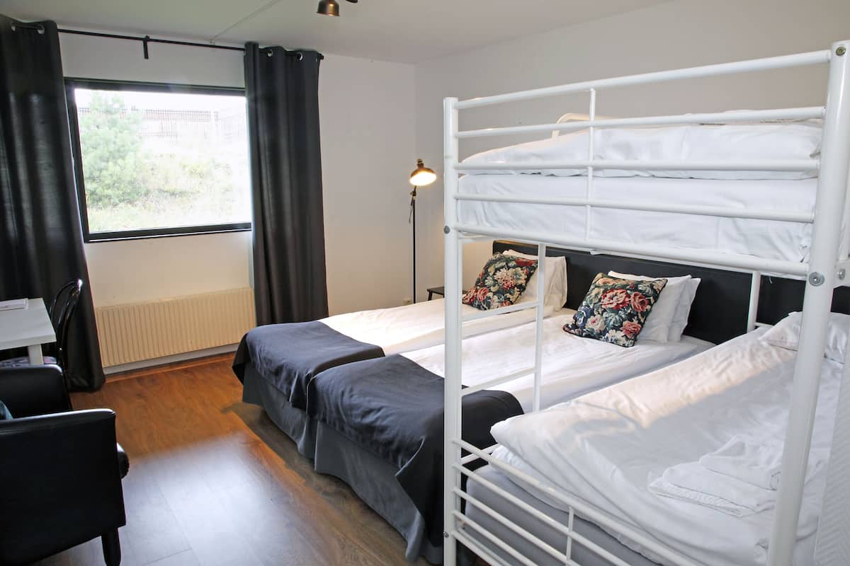 A room with two bunk beds, a desk, and a chair. There is a window with curtains, a lamp, and a radiator.