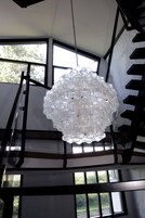 Un candelabro hecho de botellas de vidrio transparente que cuelga en un vestíbulo con ventanas amplias.