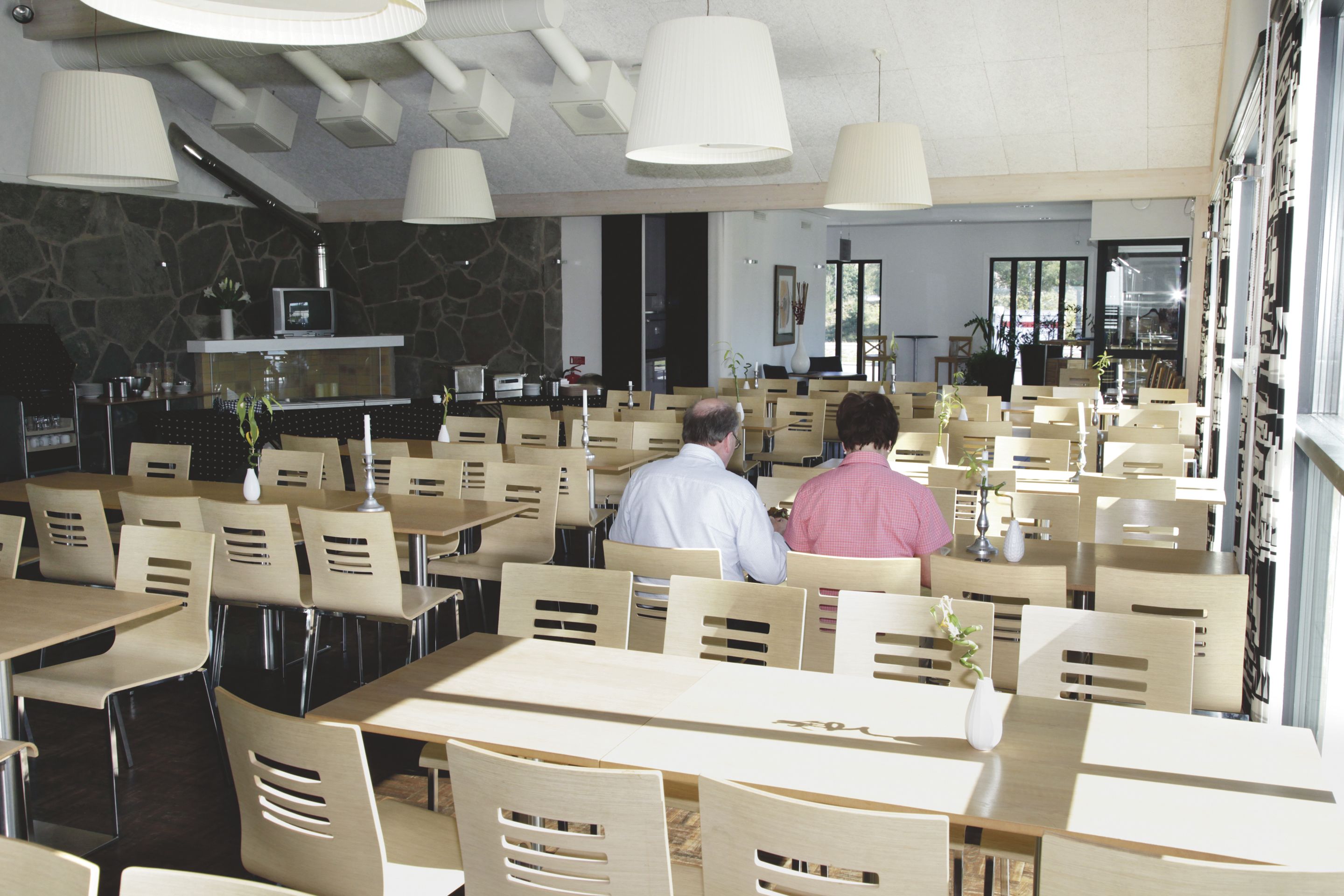 Un restaurant doté de nombreuses tables et chaises, d’un mur en pierre et de grandes lampes suspendues.